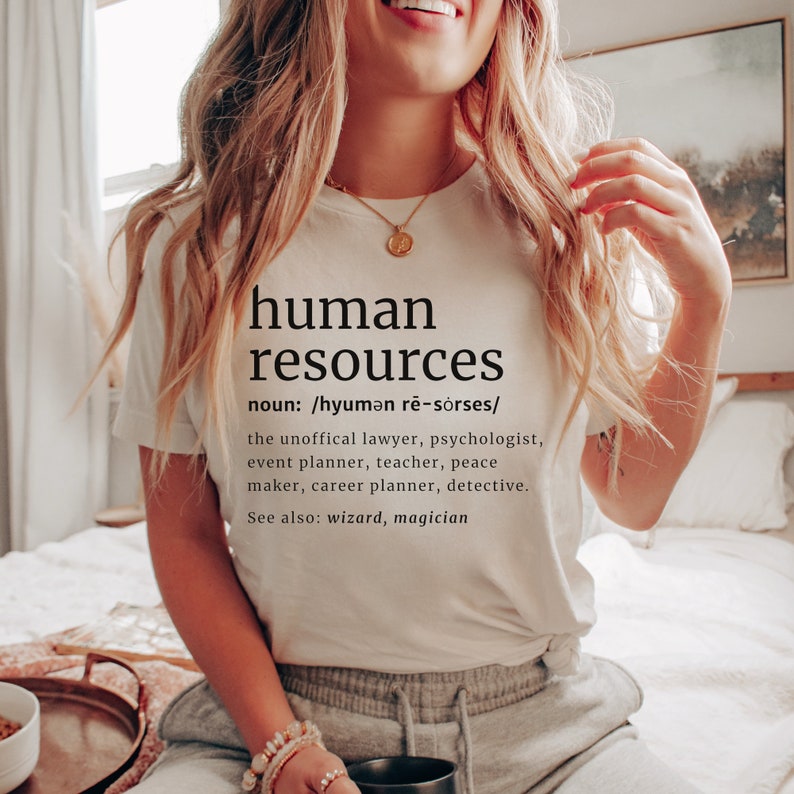 May include: Cream-colored t-shirt with the words "human resources" printed in black, along with a definition. The definition includes the roles of lawyer, psychologist, and detective. The shirt is worn by a person.
