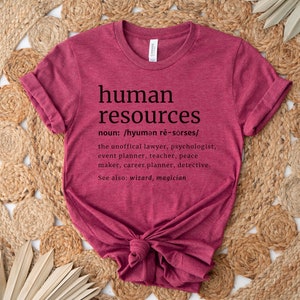 May include: A maroon t-shirt with the words "human resources" in black, along with a definition and related job titles. The shirt is knotted at the bottom and sits on a woven, beige surface.
