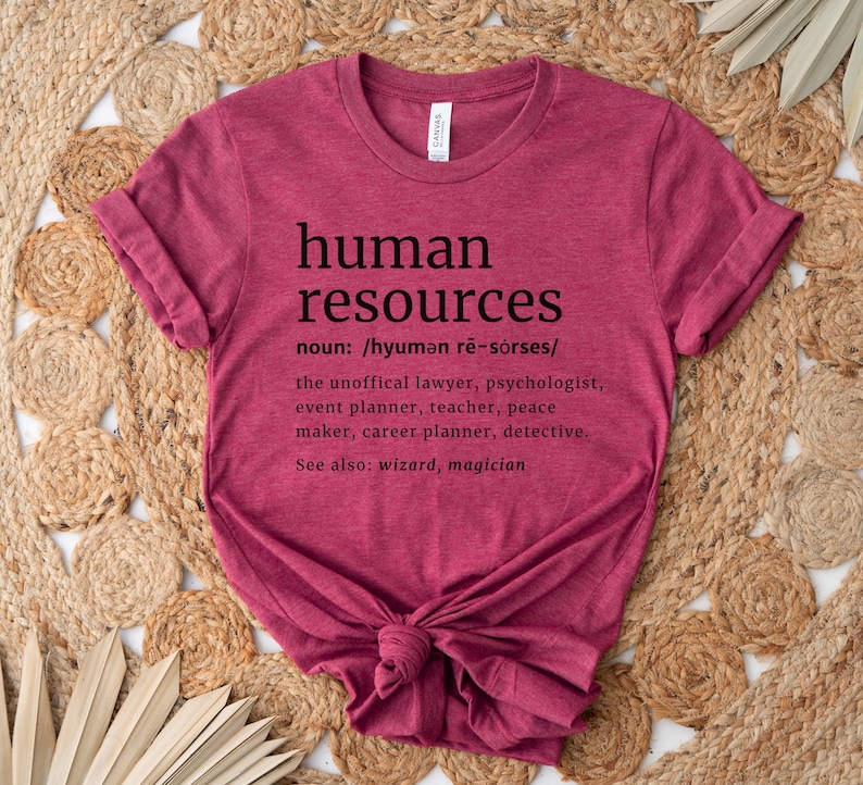 May include: A maroon t-shirt with the words "human resources" in black, along with a definition and related job titles. The shirt is knotted at the bottom and sits on a woven, beige surface.