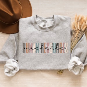 May include: Gray sweatshirt with the text "HUMAN RESOURCES" in colorful block letters and the name "michelle" written in cursive underneath.