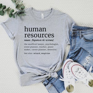 May include: A light gray t-shirt with the words "human resources" printed in black. The definition of human resources is printed below the title. The shirt is paired with blue jeans and white sneakers.