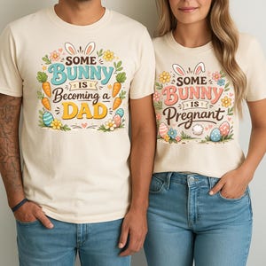 May include: Two cream-colored t-shirts with Easter-themed graphics. One shirt says "Some Bunny is Becoming a Dad" with bunny ears, carrots, and Easter eggs. The other says "Some Bunny is Pregnant" with similar imagery.