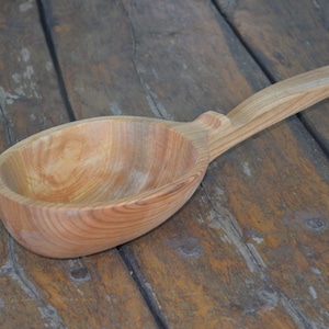 May include: A large wooden ladle with a long handle. The ladle is made of light brown wood and has a smooth, rounded bowl.
