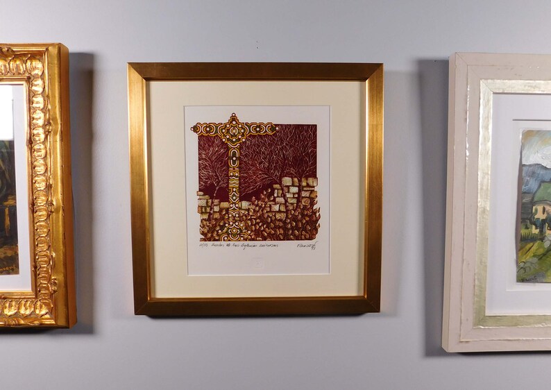 May include: A framed print of a colorful abstract artwork depicting a cross-shaped structure with a red background. The artwork is surrounded by a gold frame and a white mat.