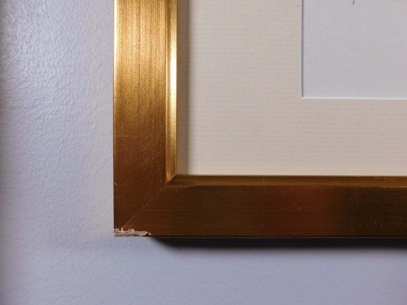 May include: Close-up of a gold picture frame with a slight chip on the corner.