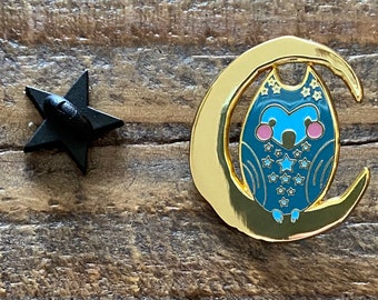 May include: Gold enamel pin featuring a blue owl with white stars sitting on a crescent moon.