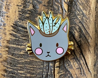 May include: A grey cat with a cute face wearing a gold crown with a green succulent plant inside. The cat is wearing a gold crown with a green succulent plant inside.