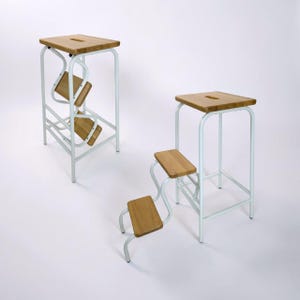 Puede incluir: Tres taburetes modernos con marcos de metal blanco y asientos de madera. Los taburetes tienen un diseño único con soportes curvos y una parte superior rectangular. Los asientos son de madera clara. Los taburetes están diseñados para la funcionalidad y el estilo.