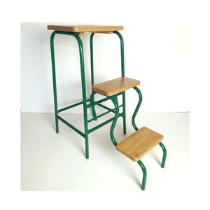 Puede incluir: Un taburete de metal verde con tres escalones de madera. El escalón superior es rectangular y los dos escalones inferiores son más pequeños. El marco es de color verde brillante y la madera tiene un acabado natural.