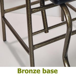 Op de afbeelding: Close-up van een bronzen metalen stoelbasis. De basis heeft een getextureerde afwerking en een netwerk van elkaar kruisende staven en gebogen steunen. De tekst "Bronze base" staat onderaan de afbeelding.