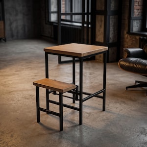 Op de afbeelding: Een vierkant houten tafelblad ondersteund door een zwart metalen frame met een geïntegreerde lagere houten trede. De structuur heeft een hoog, smal ontwerp met strakke lijnen, waarbij natuurlijke lichtgekleurde houten oppervlakken worden gecombineerd met een donkere metalen basis.
