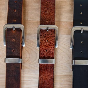 May include: Three leather belts with silver buckles. The belts are brown, orange, and black.