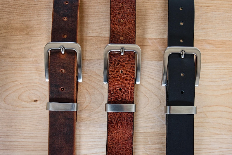 May include: Three leather belts with silver buckles. The belts are brown, orange, and black.