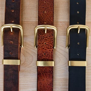 May include: Three leather belts with brass buckles. The belts are brown, red, and black.
