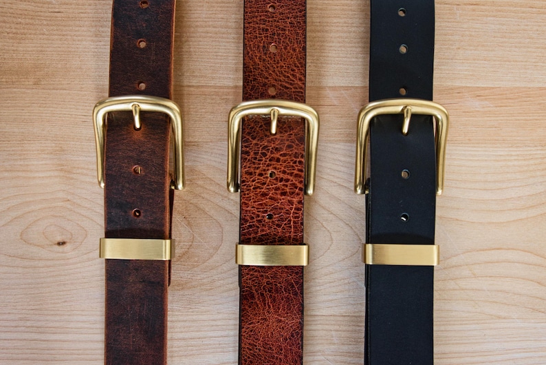 May include: Three leather belts with brass buckles. The belts are brown, red, and black.