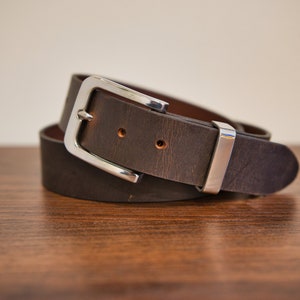 May include: A brown leather belt with a silver buckle. The belt is folded in half and the buckle is visible.