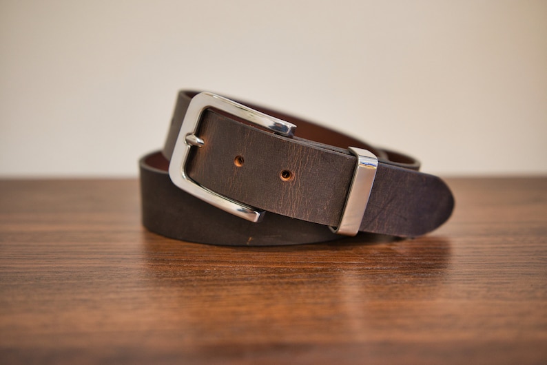 May include: A brown leather belt with a silver buckle. The belt is folded in half and the buckle is visible.