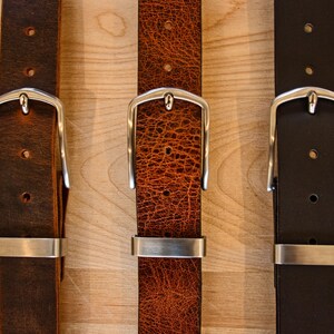 May include: Three leather belts with silver buckles. The belts are brown, orange, and black.