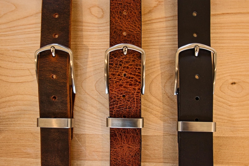 May include: Three leather belts with silver buckles. The belts are brown, orange, and black.