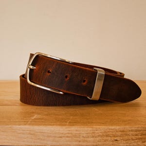 May include: A brown leather belt with a silver buckle. The belt is rolled up and the buckle is visible.