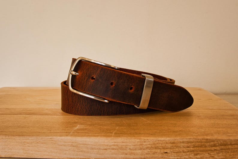 May include: A brown leather belt with a silver buckle. The belt is rolled up and the buckle is visible.