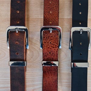 May include: Three leather belts with silver buckles. The belts are brown, red, and black.