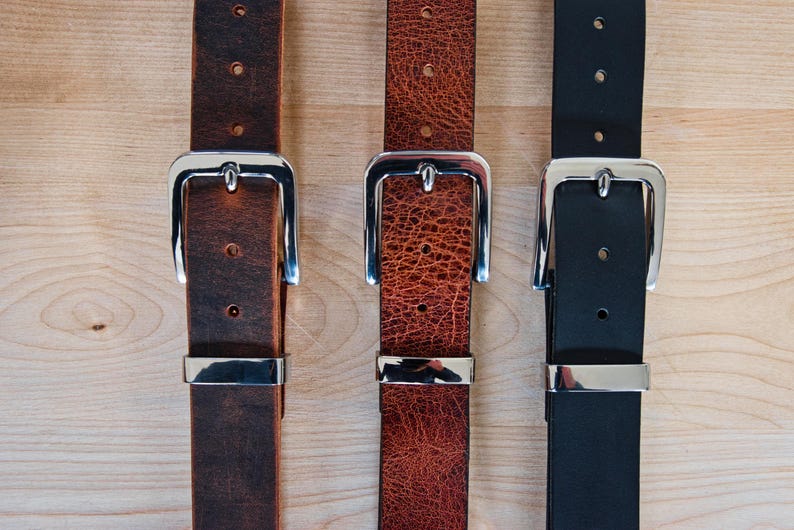 May include: Three leather belts with silver buckles. The belts are brown, red, and black.