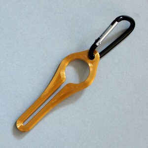 Puede incluir: Un llavero de metal de color dorado con un mosquet&oacute;n negro. El llavero tiene forma de anillo con un peque&ntilde;o bucle en la parte superior.