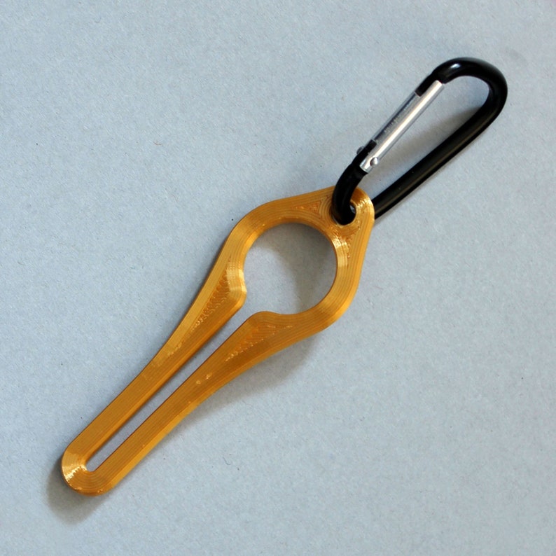 Puede incluir: Un llavero de metal de color dorado con un mosquet&oacute;n negro. El llavero tiene forma de anillo con un peque&ntilde;o bucle en la parte superior.