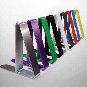 May include: A collection of colorful bookends in various shades, including silver, purple, green, black, white, gray, red, blue, and yellow. Each bookend has a flat base and a curved, angled support.
