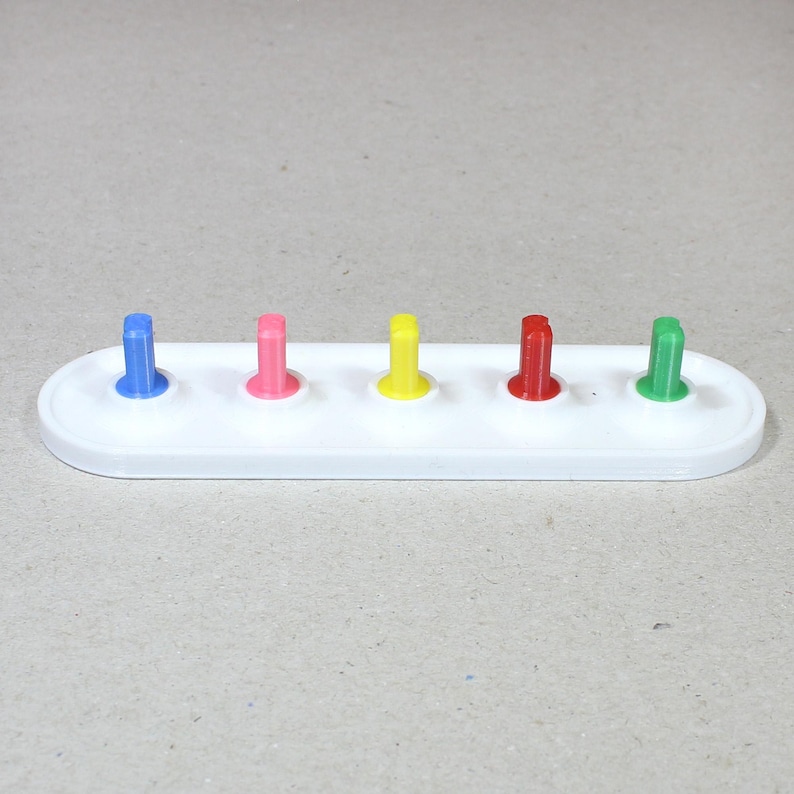 May include: A white plastic base with five colored pegs. The pegs are blue, pink, yellow, red, and green.