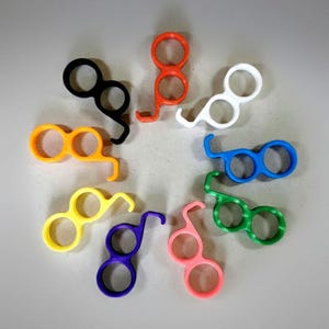 May include: A collection of colorful, plastic finger-sized tools in various colors, including black, orange, white, blue, green, yellow, purple, and pink. Each tool has two circular openings and a curved hook.