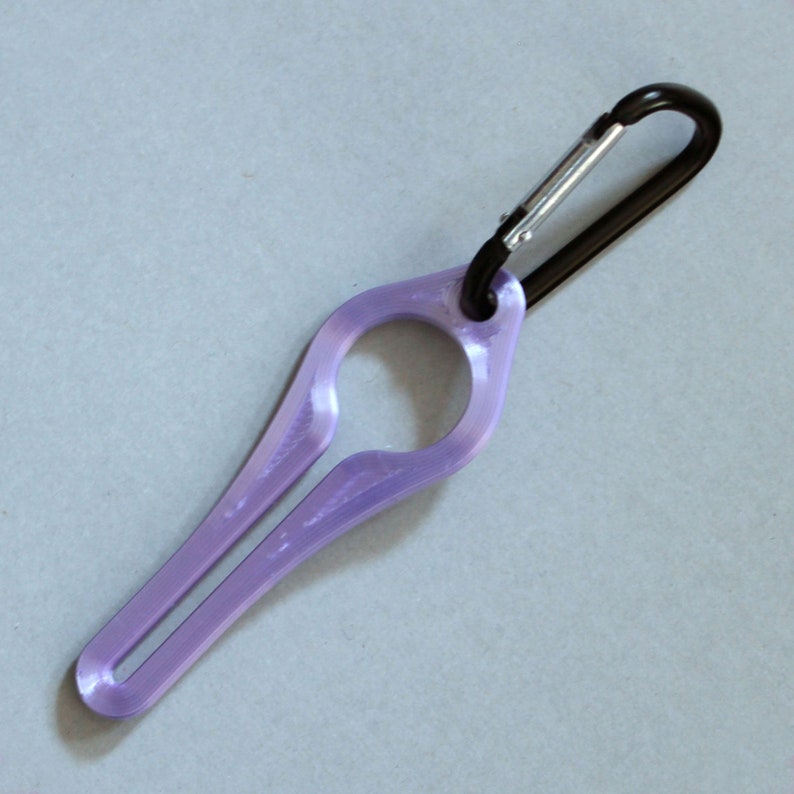 Puede incluir: Un llavero de pl&aacute;stico morado con un mosquet&oacute;n negro. El llavero tiene forma de anillo con una peque&ntilde;a abertura en el centro.