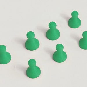 May include: Seven green game pieces arranged on a white surface. Each piece has a rounded base and a smaller, rounded top, resembling a person. The pieces are evenly spaced, creating a pattern.