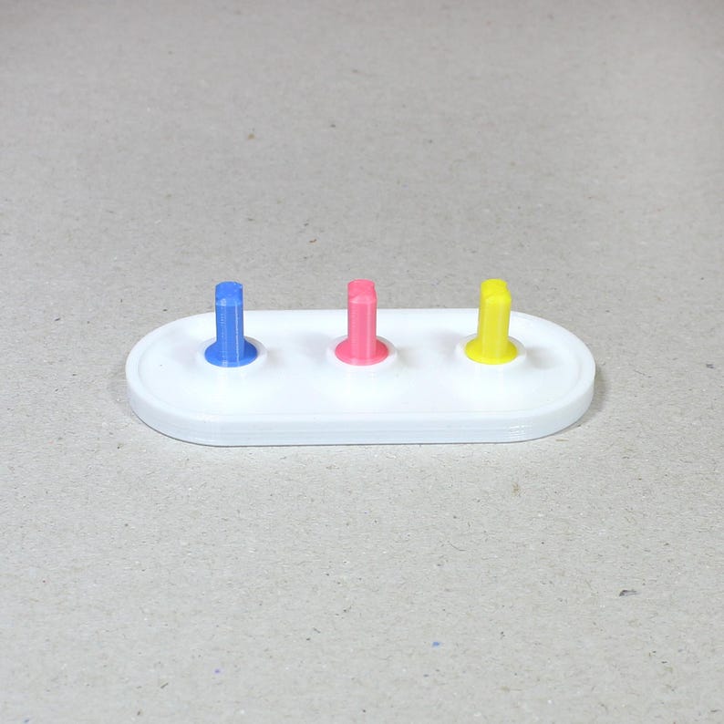 May include: A white plastic base with three colored pegs. The pegs are blue, pink, and yellow.