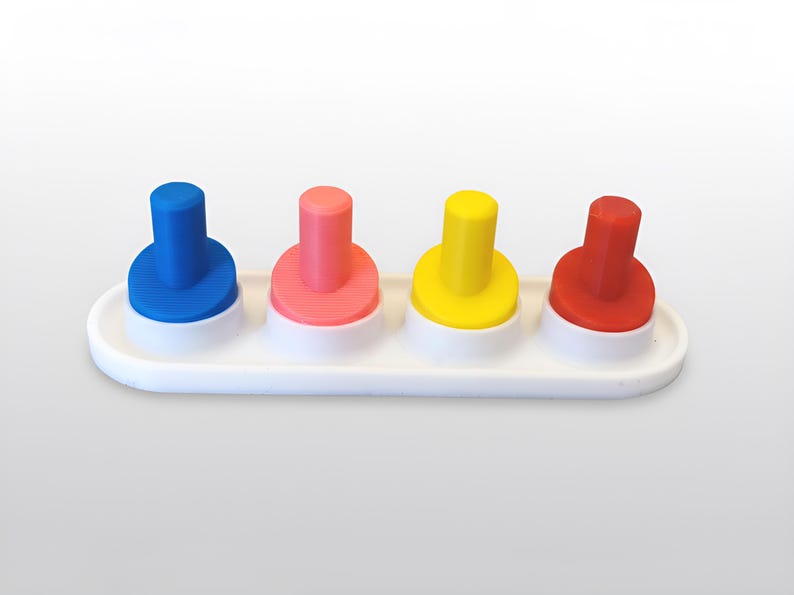 May include: A white plastic tray holds four colorful pegs: blue, pink, yellow, and red. Each peg has a cylindrical top and a circular base. The bases are white, and the tray is also white.