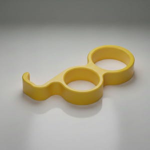 May include: A yellow bottle opener with a unique design. It features two circular openings connected by a curved handle and a hook-shaped end. The opener is made of a solid, smooth material.