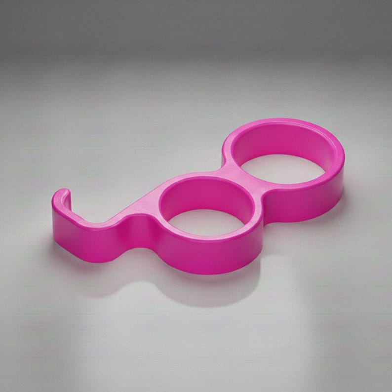 May include: A bright pink, plastic bottle opener with two circular openings and a curved hook. The design is a solid, one-piece construction, casting a shadow on a neutral background. The opener is designed for easy grip and leverage.