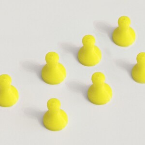 May include: Seven bright yellow game pieces, each with a rounded base and a bulbous top, are arranged on a white surface. The pieces are evenly spaced, creating a visually appealing pattern. The objects are likely for a board game.