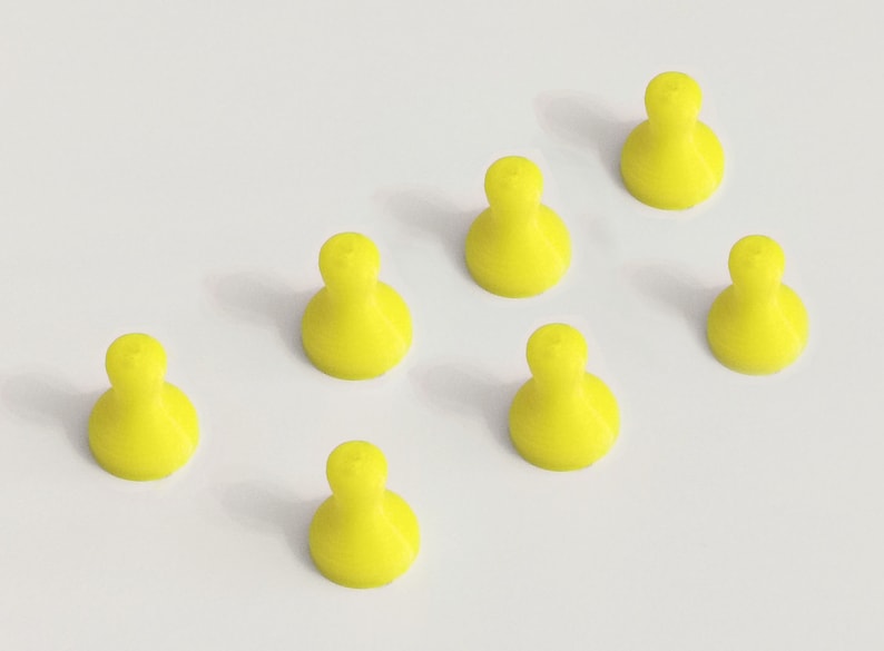 May include: Seven bright yellow game pieces, each with a rounded base and a bulbous top, are arranged on a white surface. The pieces are evenly spaced, creating a visually appealing pattern. The objects are likely for a board game.