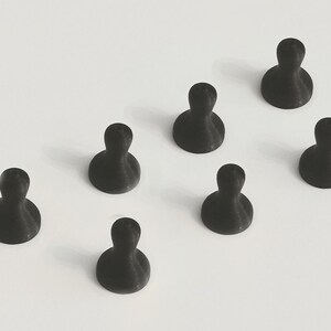 May include: Seven black push pins arranged on a white surface. Each pin has a rounded base and a cylindrical top, resembling a small person. The pins are evenly spaced and angled slightly.