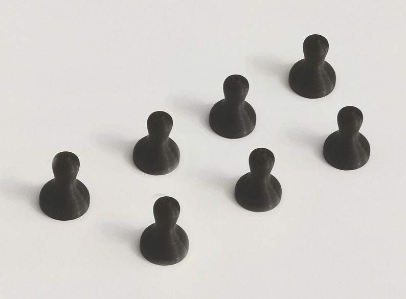 May include: Seven black push pins arranged on a white surface. Each pin has a rounded base and a cylindrical top, resembling a small person. The pins are evenly spaced and angled slightly.