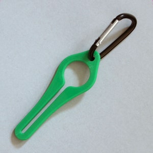 Puede incluir: Un porta botellas de pl&aacute;stico verde con un mosquet&oacute;n negro. El porta botellas tiene un bucle para sujetar una botella y un mango largo y delgado.