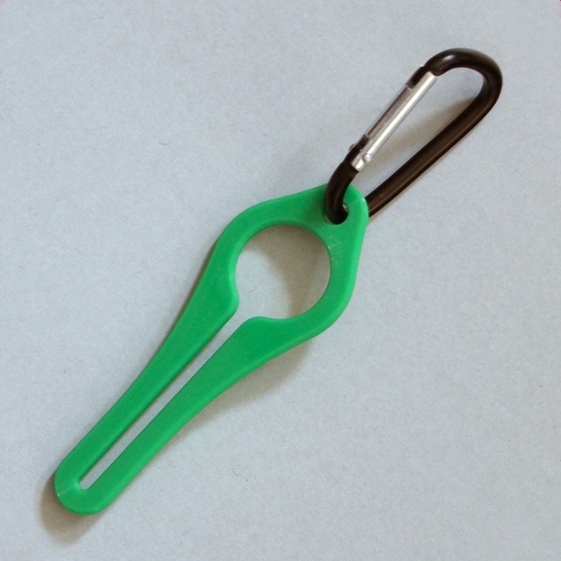 Puede incluir: Un porta botellas de pl&aacute;stico verde con un mosquet&oacute;n negro. El porta botellas tiene un bucle para sujetar una botella y un mango largo y delgado.