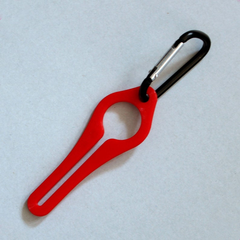 Puede incluir: Un llavero de pl&aacute;stico rojo con un mosquet&oacute;n negro. El llavero tiene un bucle en la parte superior y un extremo largo, delgado y puntiagudo.