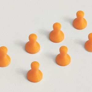 May include: Seven orange, abstract-shaped game pieces are arranged on a white surface. Each piece has a rounded base and a smaller, rounded top. The pieces are evenly spaced, creating a visually appealing pattern.