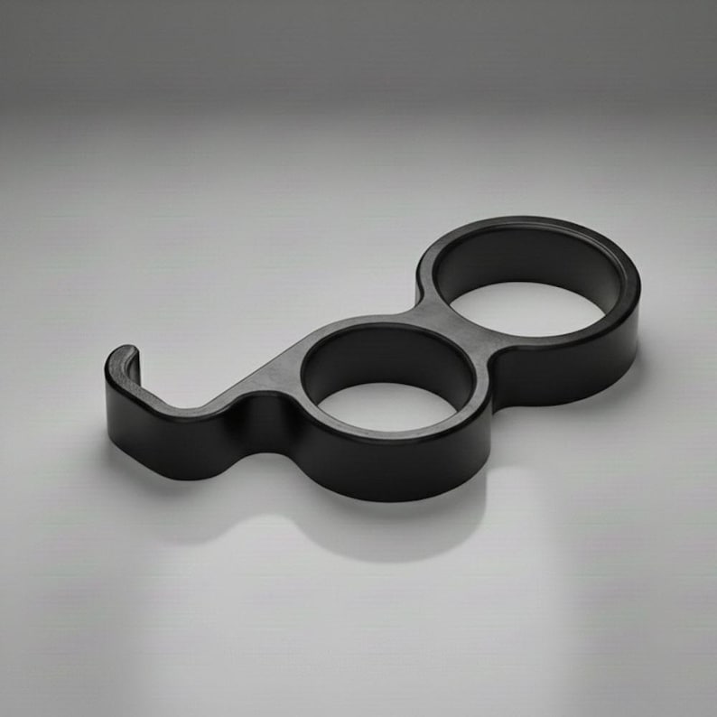 May include: A black, sculptural bottle opener with a unique design. It features two circular openings and a curved hook, all in a matte finish. The opener is designed for easy handling and a modern aesthetic.