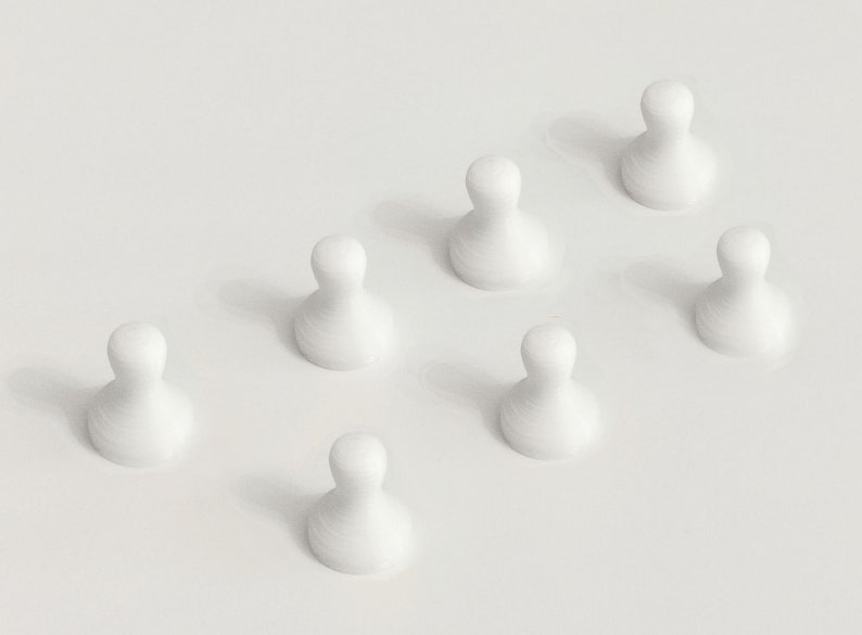 May include: Seven white, teardrop-shaped game pieces arranged in a diagonal pattern. The pieces have a smooth, rounded top and a wider base, casting soft shadows on a white surface. The overall aesthetic is minimalist and clean.