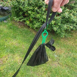 Puede incluir: Un dispensador de bolsas para excrementos de perros de pl&aacute;stico negro con un clip de pl&aacute;stico verde unido a una correa negra.