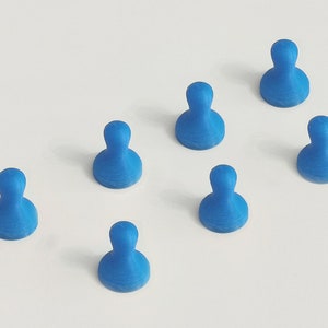 May include: Seven blue push pins arranged on a white surface. Each pin has a rounded top and a wider base, resembling a person-shaped design. The pins are evenly spaced, creating a visually appealing pattern.